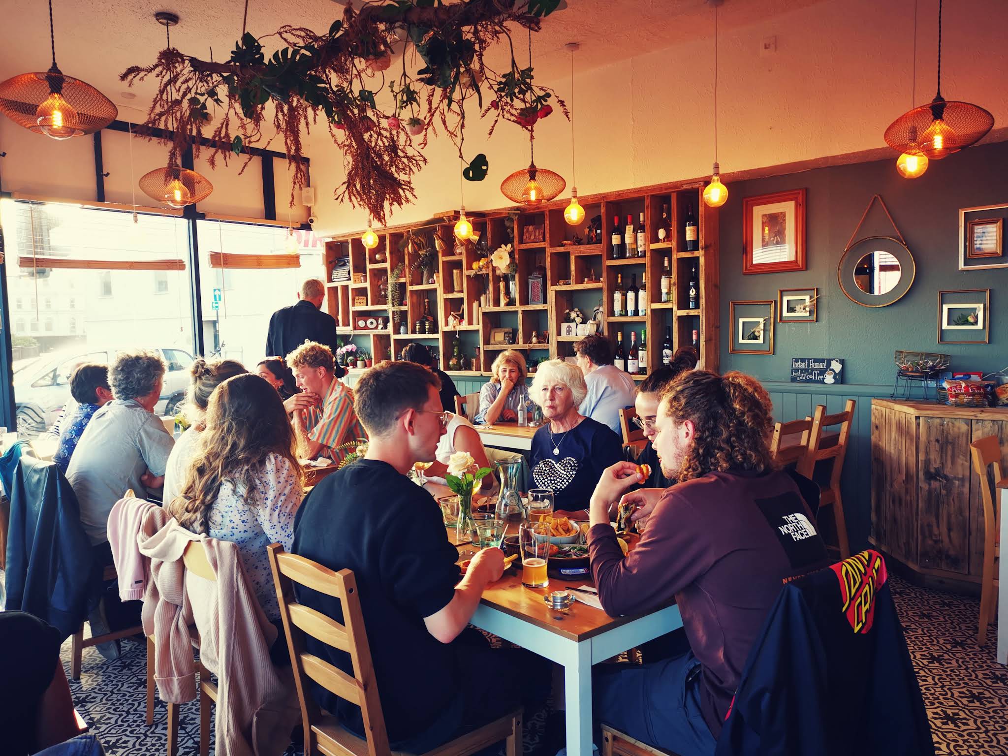 Yaaze interior with warm pendant lights, wooden shelving, teal walls and people at tables